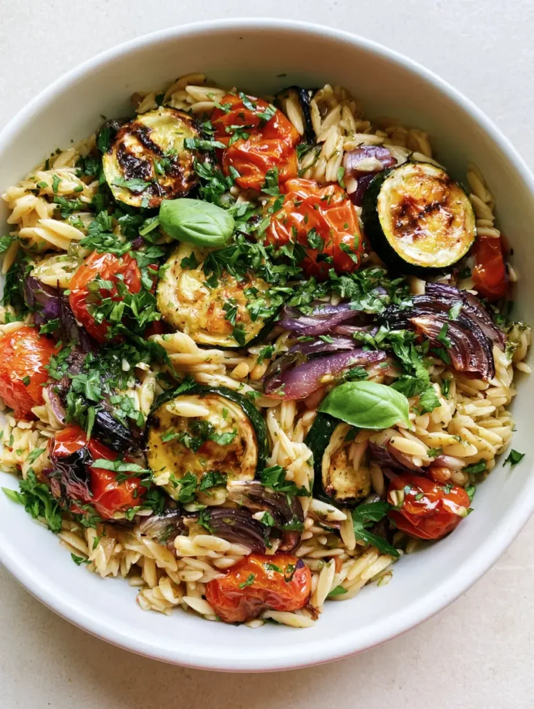 Nahaufnahme von Orzo-Salat mit Röstgemüse, glänzenden Zucchini und saftigen Cherrytomaten.
