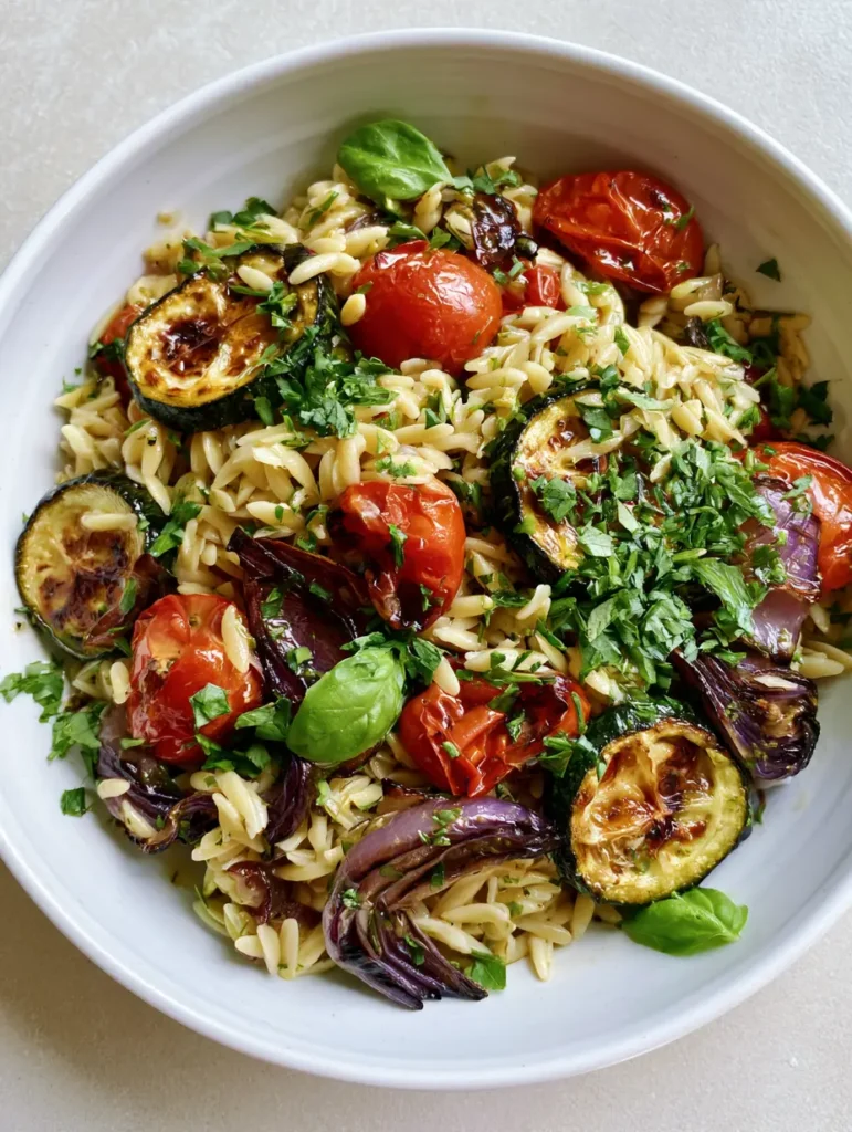 Draufsicht auf eine weiße Schüssel mit Orzo-Salat mit Röstgemüse und frischen Kräutern.