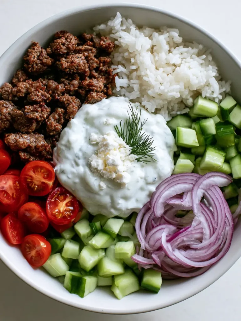Sektionsweise angerichtete Zutaten der Lamm-Gyro-Bowl: Fleisch, Reis, Gemüse.
