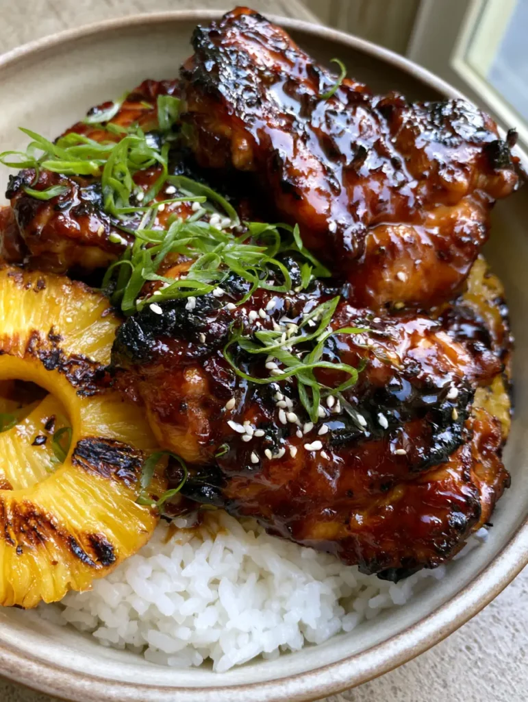 Gegrilltes Huli Huli Hähnchen serviert mit zwei gegrillten Ananasringen auf weißem Reis.