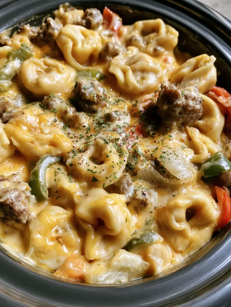 Crockpot Tortellini Rezept: Cremiges Cheesesteak-Abendessen aus dem Slow Cooker 1 Crockpot Tortellini Rezept mit geschmolzenem Käse, Petersilie und schwarzem Pfeffer im dunklen Schongarer.