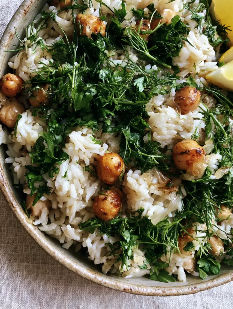 Mediterrane Reis-Pfanne serviert in einer Keramikschale mit Zitronenschnitzen auf einem Leinentuch.