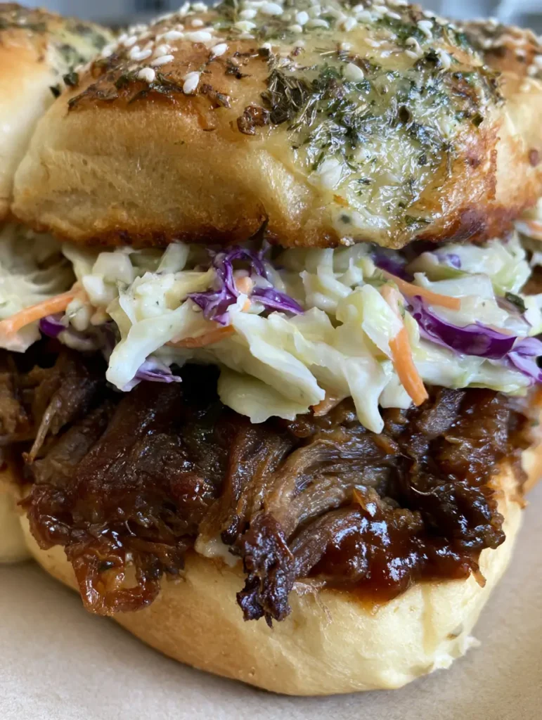 Aufsicht auf eine Auflaufform voller fertig gebackener Pulled Pork Sliders mit buntem Coleslaw.