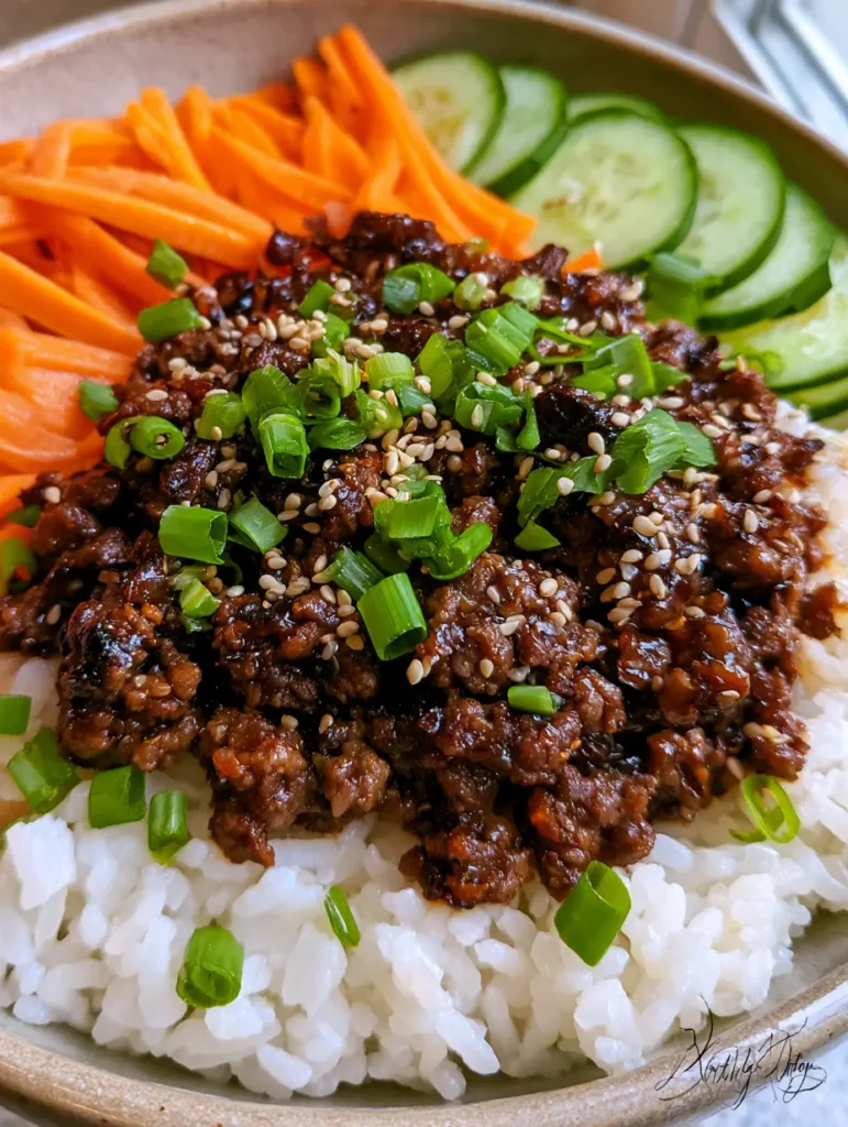 Nahaufnahme von glänzendem, karamellisiertem Rinderhackfleisch in einer Bowl mit Frühlingszwiebeln und Sesam.