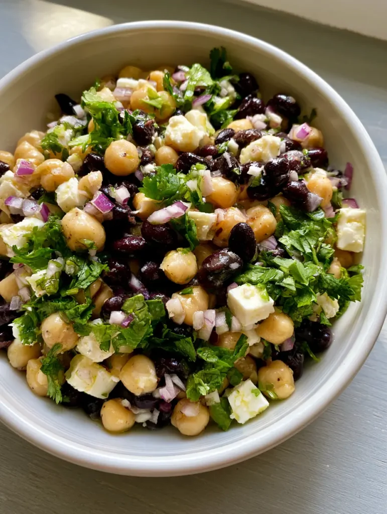 Kichererbsen-Schwarzbohnen-Salat: Das ultimative 10-Minuten-Rezept 1 Servierfertiger Kichererbsen-Schwarzbohnen-Salat auf einem hellgrauen Holztisch.